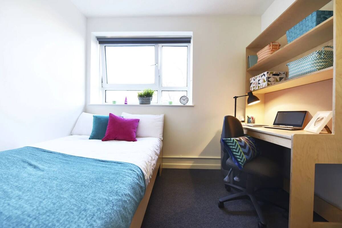 Une chambre à coucher comprenant un lit, un bureau, une chaise, une fenêtre et des étagères avec divers objets.