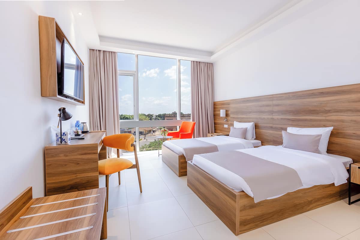 A hotel room with a large bed, a desk with a chair, a TV mounted on the wall, and a view of the outdoors.