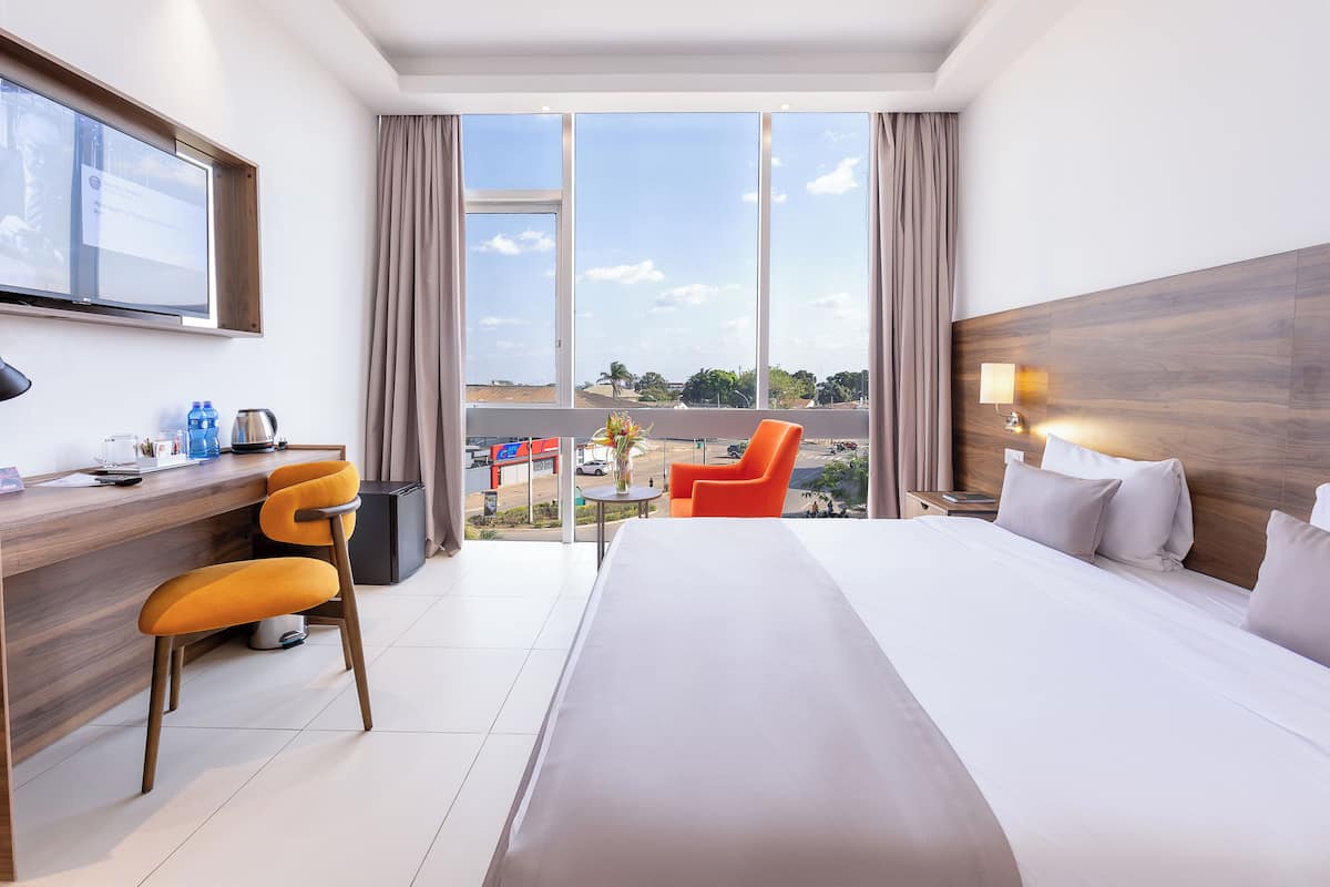 A hotel room with a large bed, a desk with a chair, a TV, and a view of the outside.