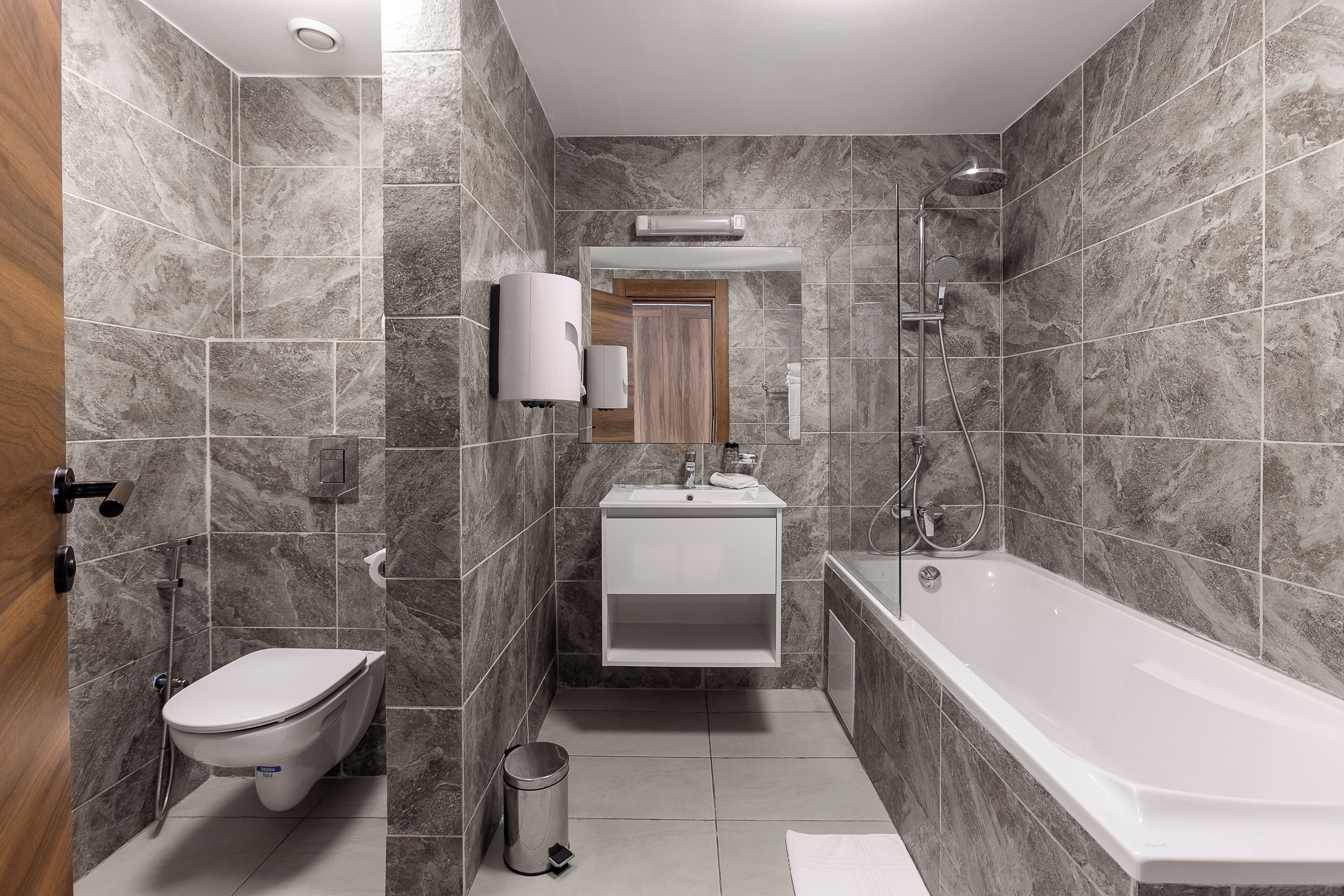 A modern bathroom with a toilet, sink, and bathtub, all set in a corner with marble tiles.