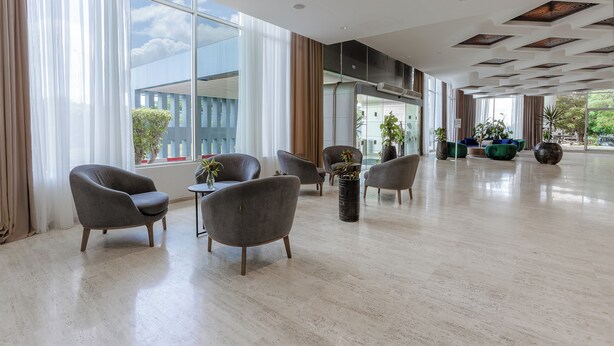A spacious lobby with large windows, modern furniture, and indoor plants.