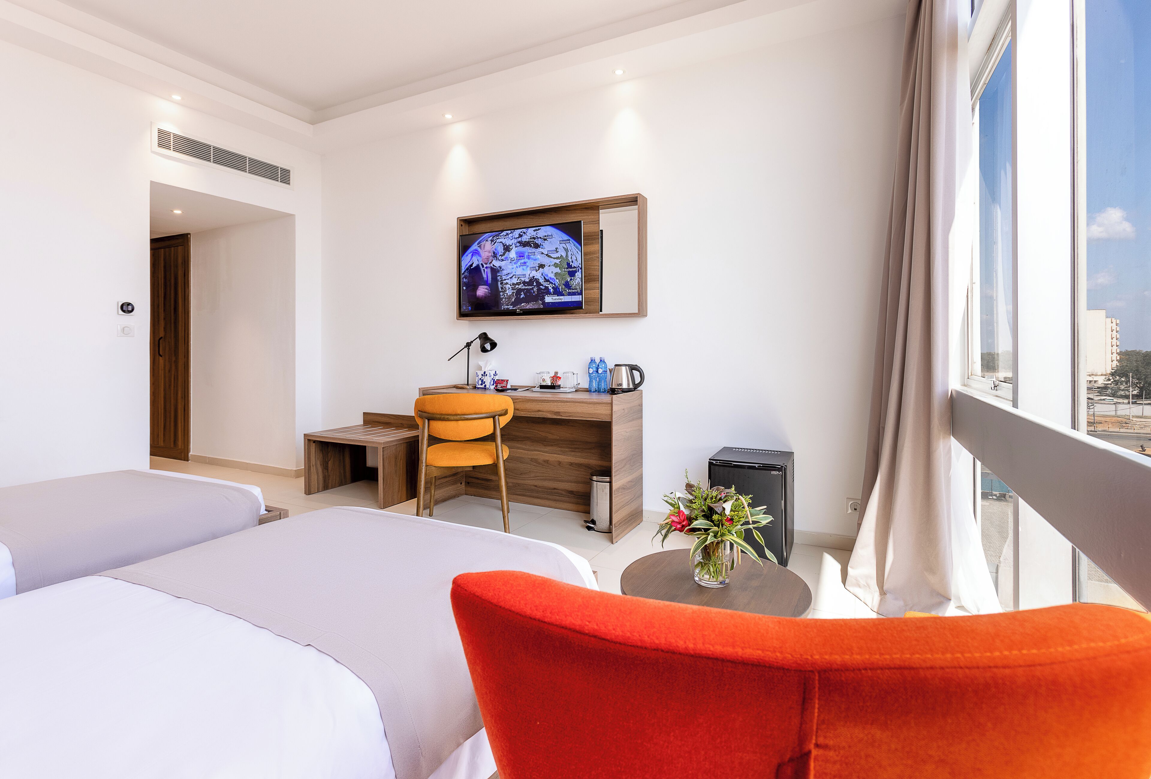 Ett hotellrum med två sängar, ett skrivbord, en stol, en TV och ett fönster med utsikt.