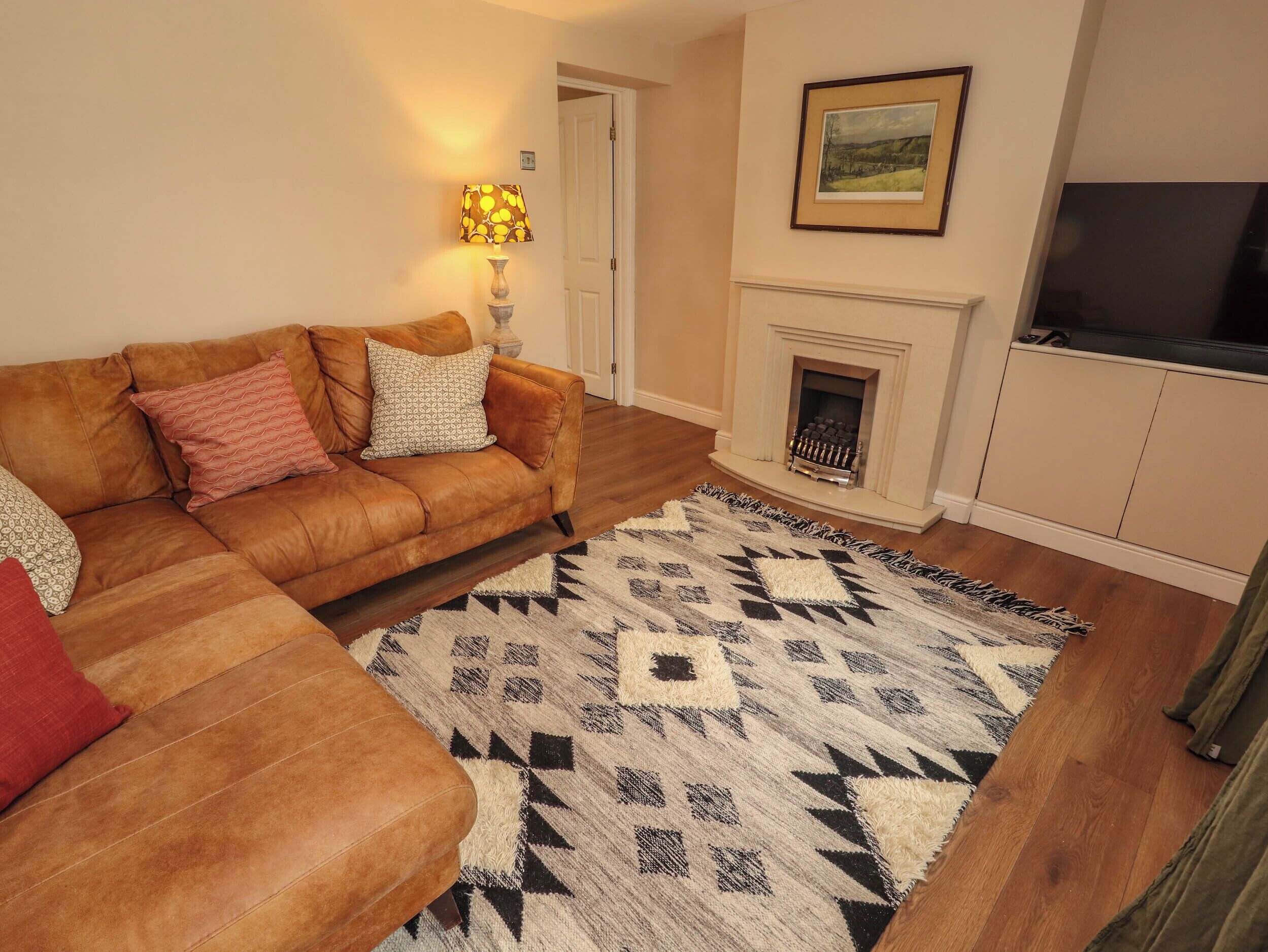 A living room with a brown leather sofa, patterned cushions, a geometric rug, a fireplace, and a framed picture on the wall.