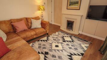 A living room with a brown leather sofa, patterned cushions, a geometric rug, a fireplace, and a framed picture on the wall.