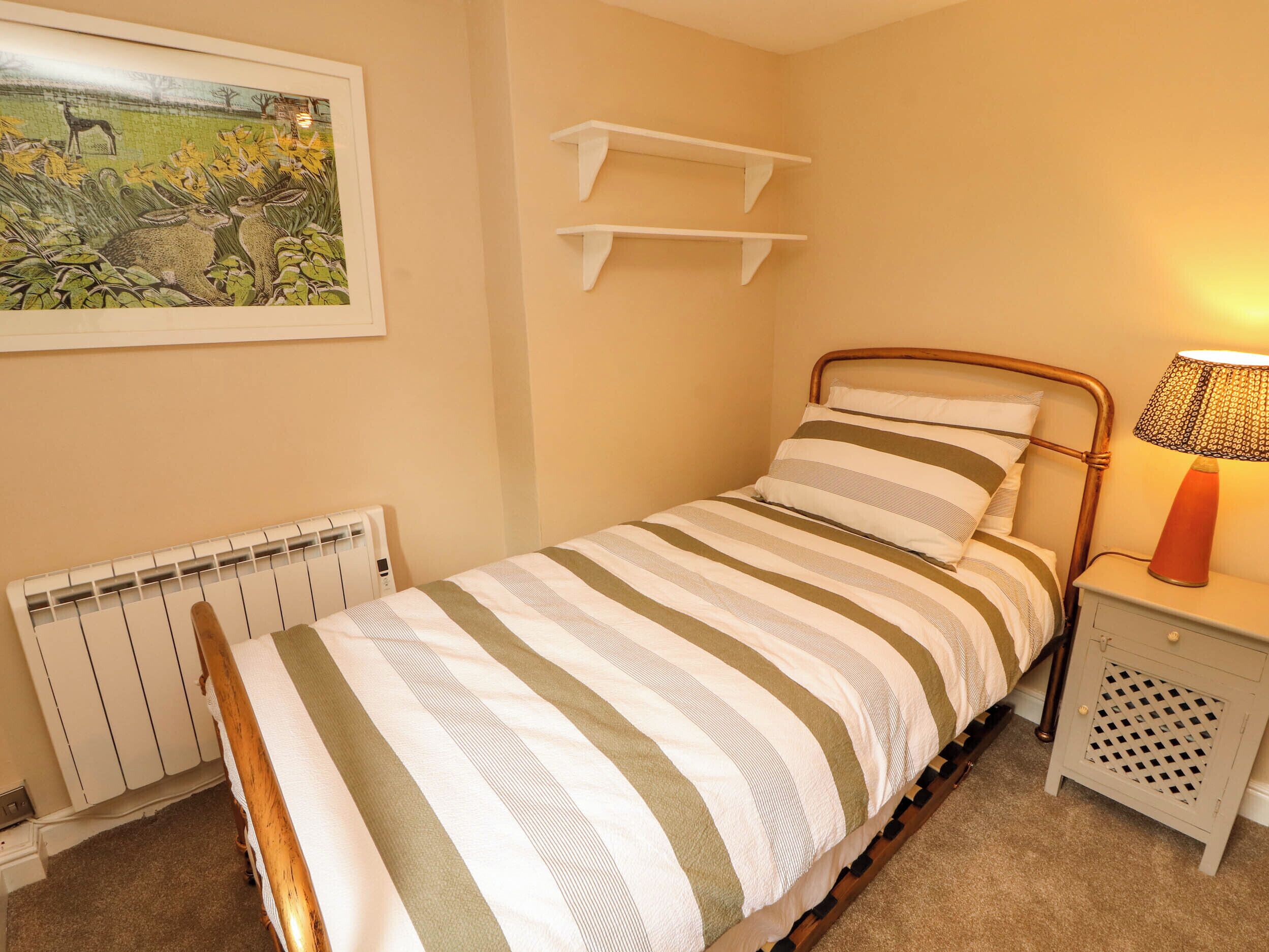 A single bed with striped bedding, a bedside lamp, a radiator, and a framed picture on the wall.