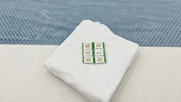 Una cama bien hecha con dos almohadas, una toalla doblada y un paquete de Medimix sobre la cama.