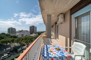 A balcony with a table set for two, overlooking a cityscape with buildings and trees. - Stylish holiday flat in poolside paradise (Lignano Sabbiadoro)