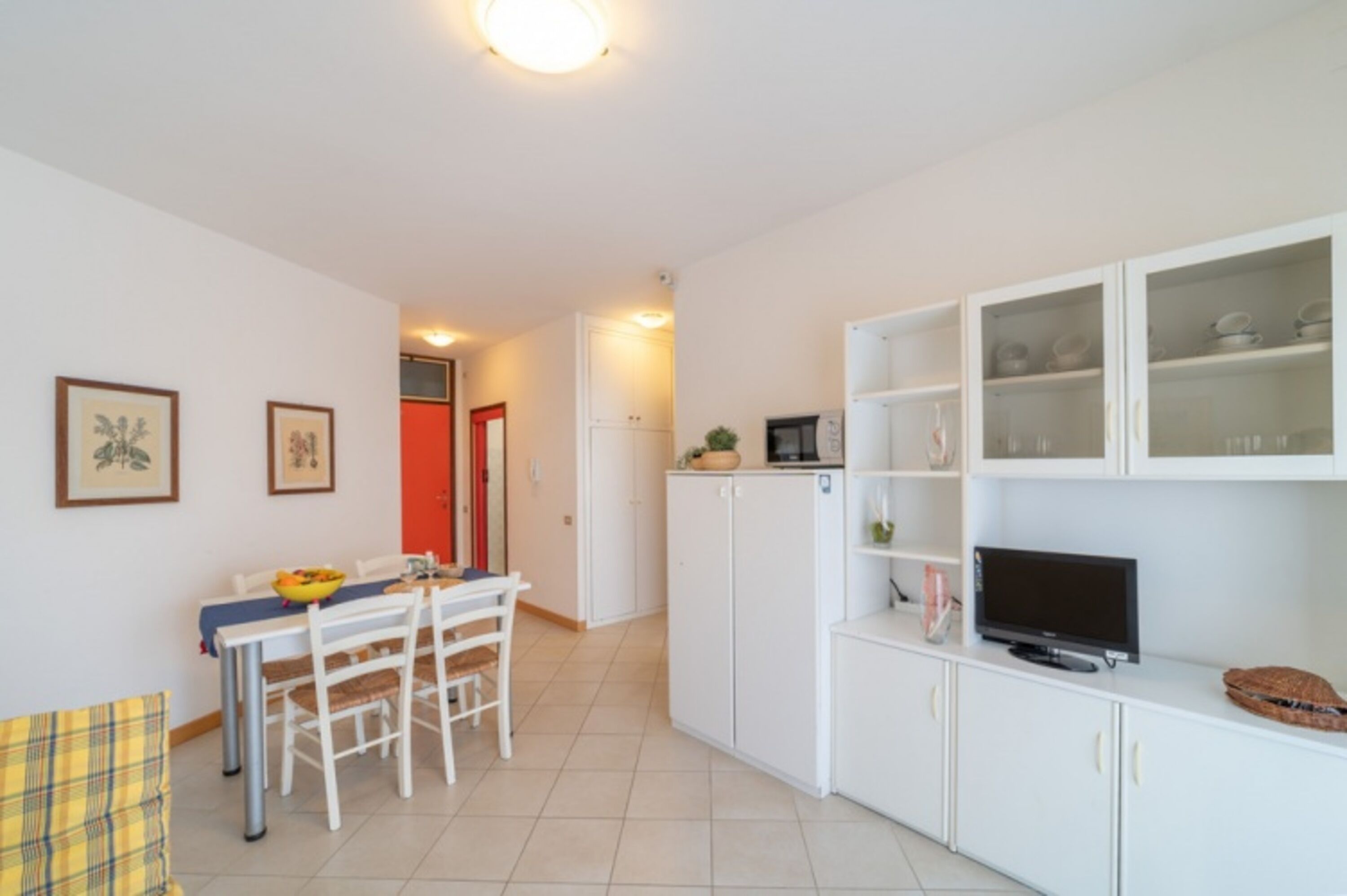 A compact kitchen with white cabinets, a dining table with chairs, a television, and a microwave.