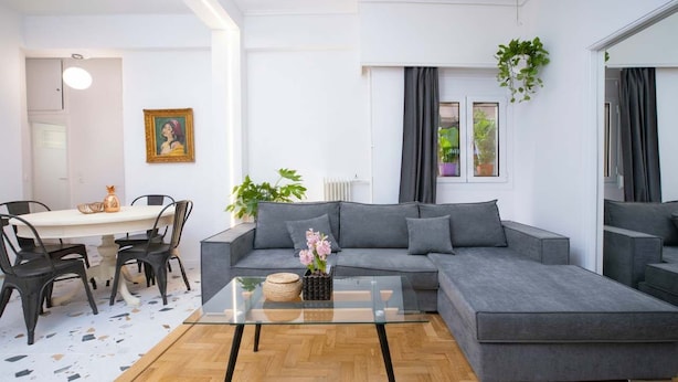 En moderne stue med en grå hjørnesofa, et glasbord og et spiseområde med et hvidt bord og sorte stole.