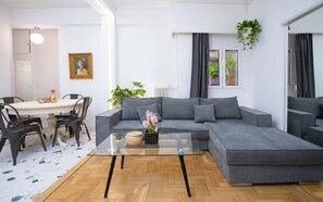 Una sala de estar moderna con un sofá seccional gris, una mesa de centro de vidrio y un comedor con mesa blanca y sillas negras.