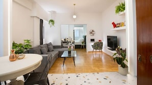 En moderne stue med sofa, sofabord og fjernsyn. Der er planter og en bogreol.
