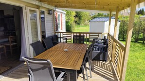 Eine überdachte Terrasse mit Holztisch und -stühlen, einer Schiebetür und Blick auf einen Garten.