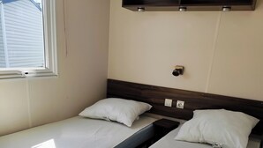 Ein Zimmer mit zwei Einzelbetten, einem Holzkopfende, einem Fenster und einem an der Wand befestigten Regal.