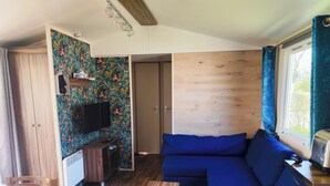 Ein gemütlicher Wohnraum mit einem blauen Sofa, Holzboden, einem kleinen Tisch und einem an der Wand montierten Fernseher.