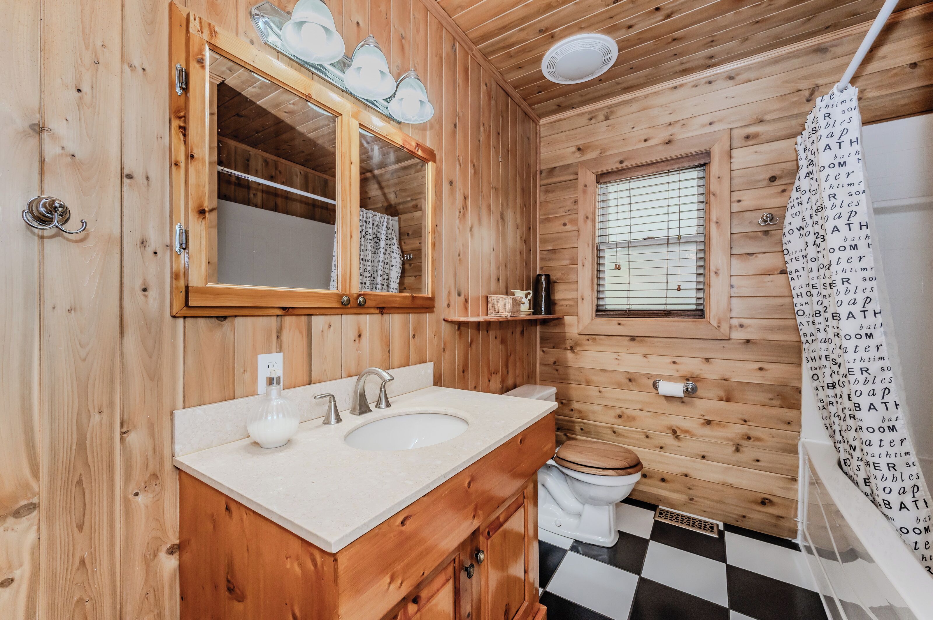 Un baño de cabaña de madera con un espejo grande, dos lavamanos, un inodoro y una cortina de ducha con texto.