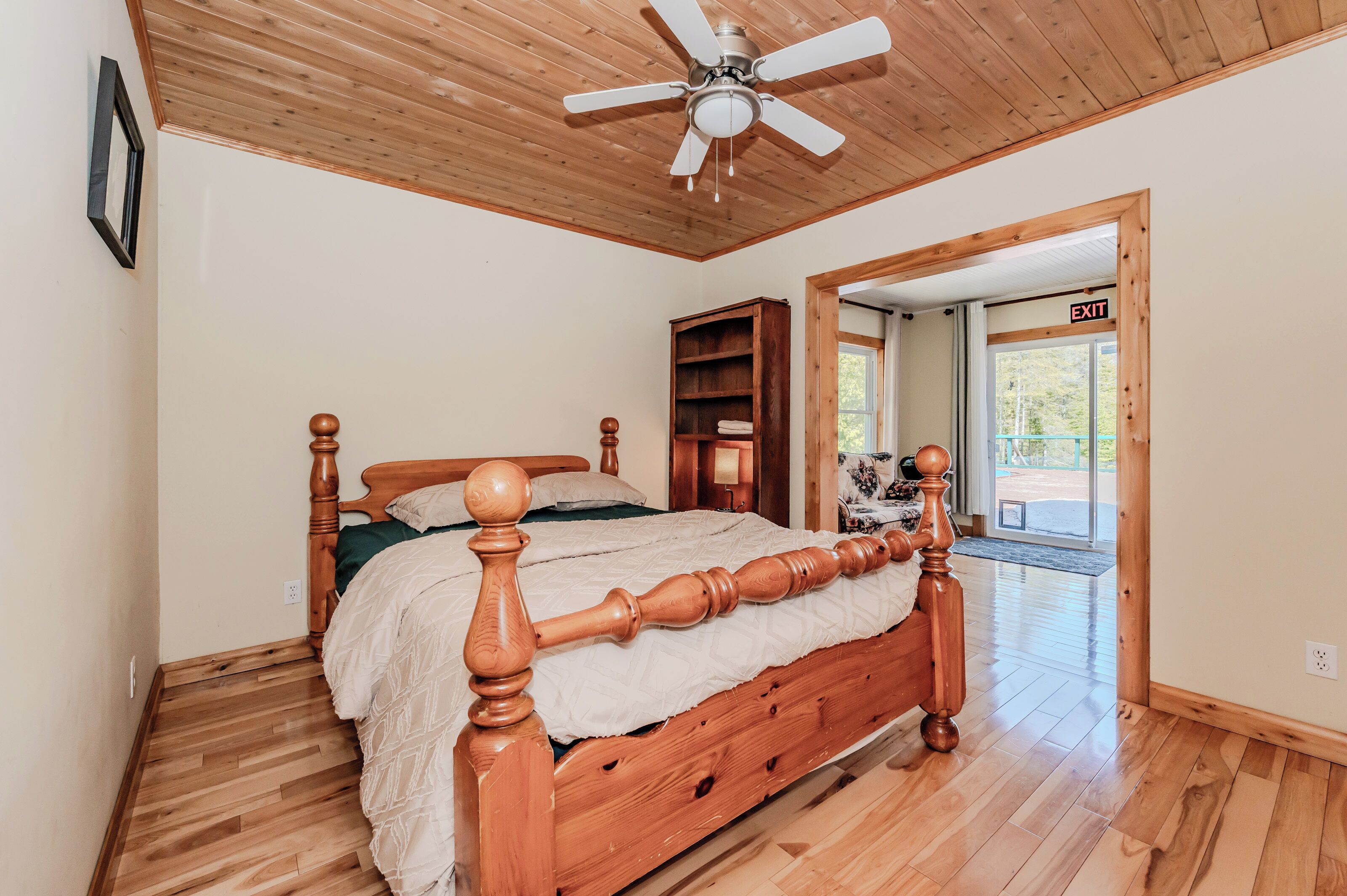 Een slaapkamer met een houten bed, een plafondventilator en uitzicht op de omgeving door een deur.