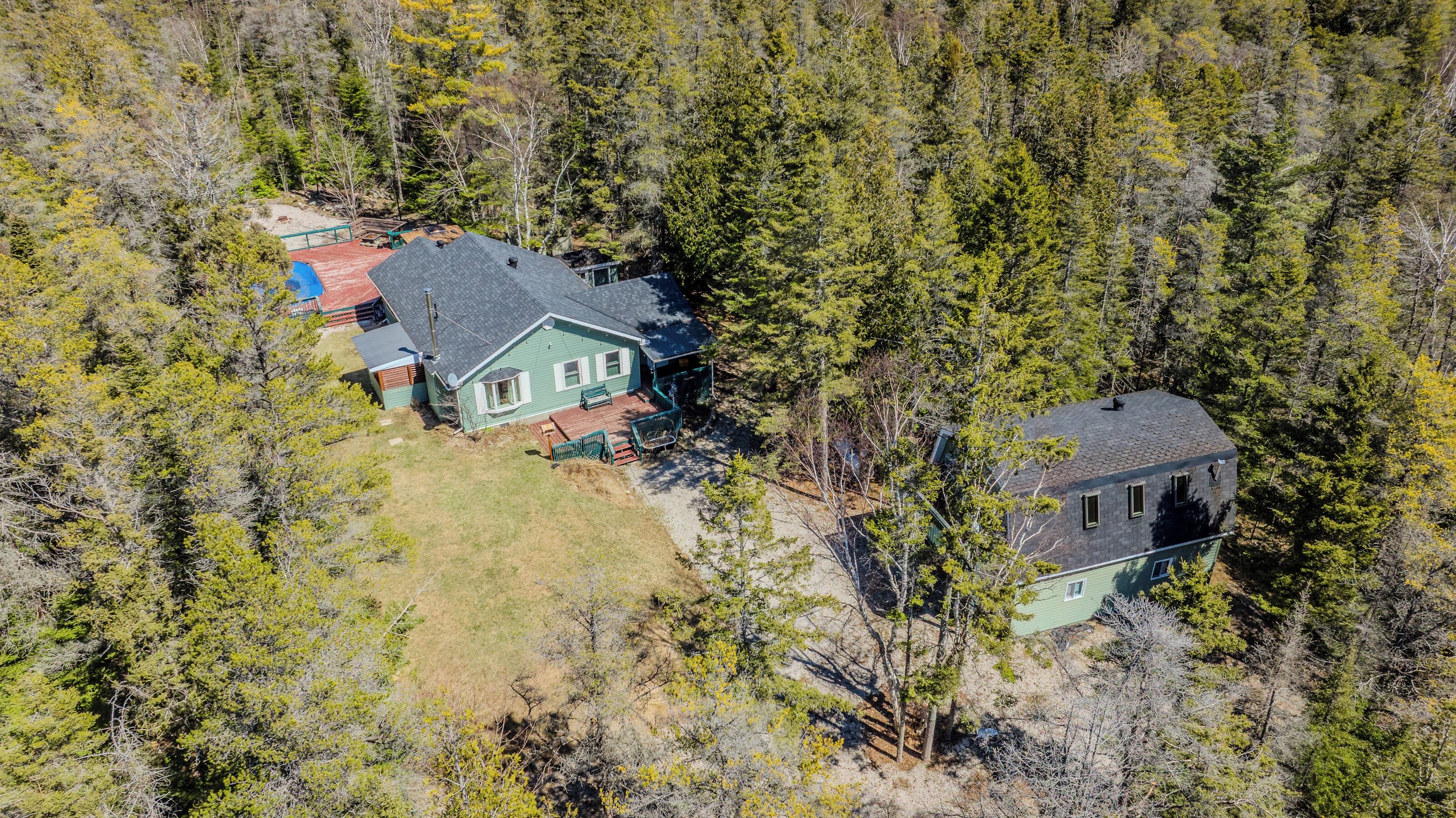A two-story house with a deck and a separate garage, surrounded by dense forest.