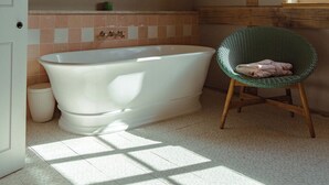 A bathroom with a freestanding bathtub, a green wicker chair, and a window allowing natural light. - Wilderness Reserve - Poachers (Halesworth)