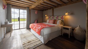A bedroom with a large bed, wooden beams, a nightstand, a lamp, and a view of the outdoors. - Wilderness Reserve - Poachers (Halesworth)