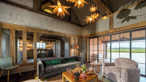 A spacious living area with a high ceiling, wooden beams, and large windows offering a view of the outdoors. - Wilderness Reserve - Poachers (Halesworth)