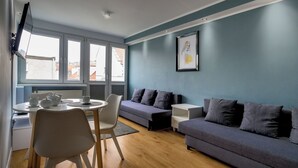 Una sala de estar moderna con un sofá gris, una mesa de comedor con sillas y una ventana con persianas.