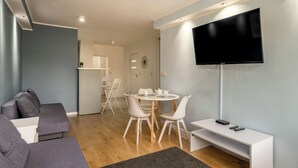 Una sala de estar moderna con un sofá, una mesa redonda con sillas, un televisor de pantalla plana y un mueble bajo en blanco.