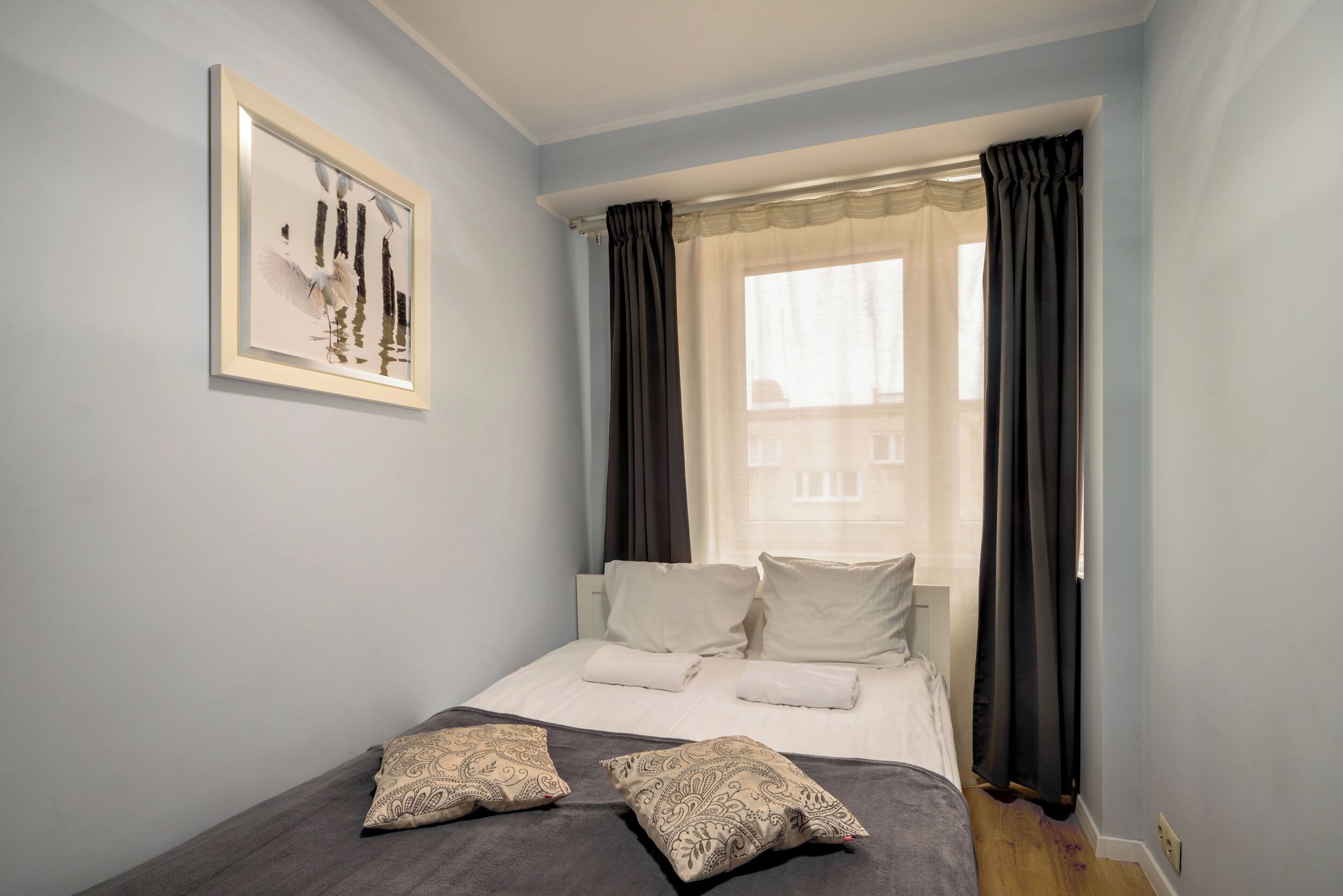 A bedroom with a bed, pillows, a framed picture on the wall, and a window with curtains.