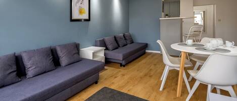 A modern living room with a grey sofa, a smaller grey sofa, a white table with chairs, and a framed picture on the wall.