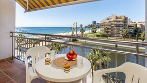 Un balcón con vista al mar, una mesa con comida y bebidas, y un toldo a rayas.