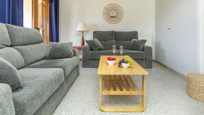 Una sala de estar moderna con dos sofás grises, una mesa de centro de madera con fruta y una lámpara fijada a la pared.