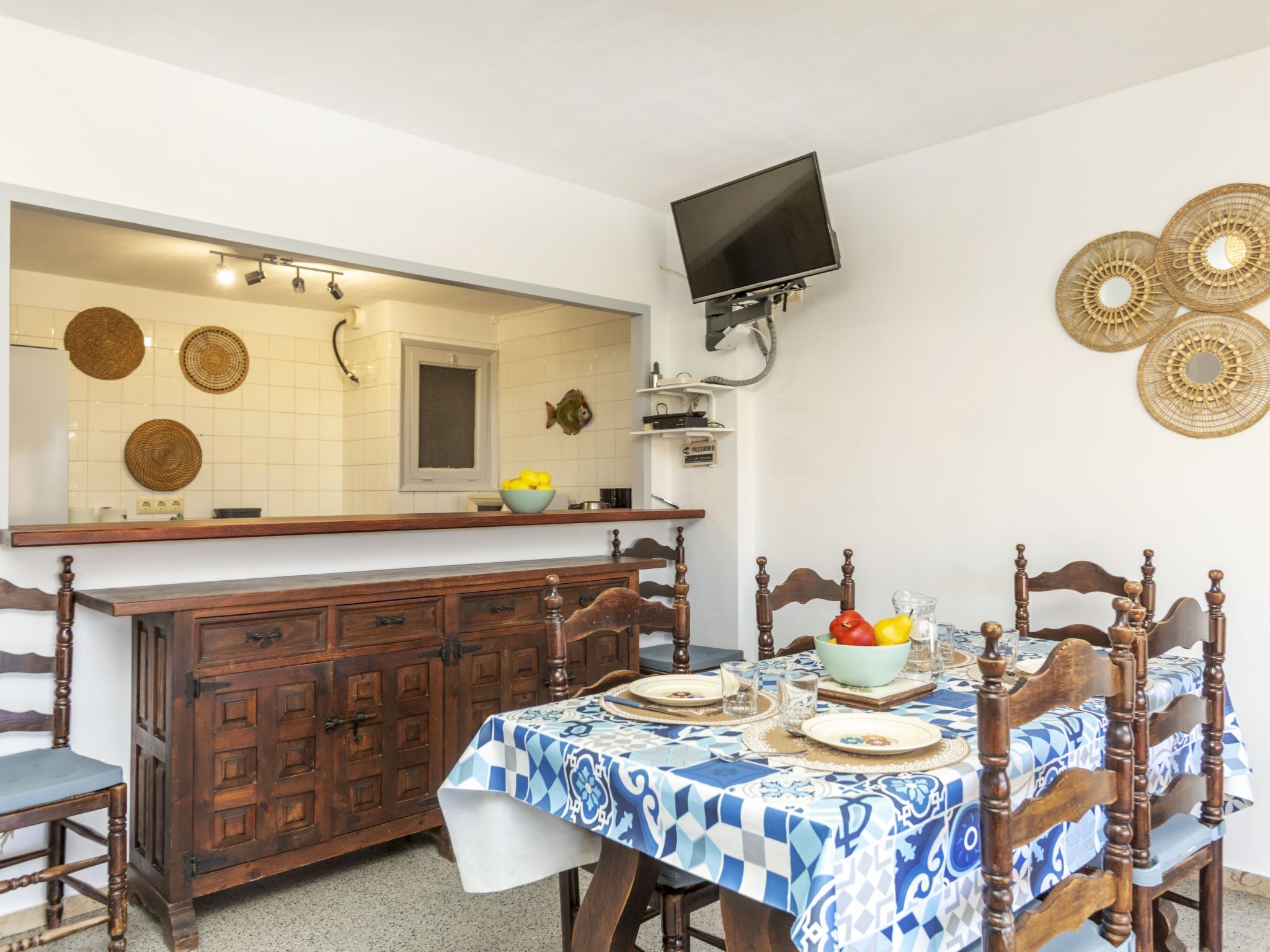 A dining area with a table set for four, a wooden cabinet, a television mounted on the wall, and decorative wall art.
