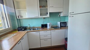 A compact kitchen with white cabinets, a wooden countertop, a sink, a kettle, a microwave, and a trash bin. - Vue MER bleu sea beach Holidays tramway (Nice)