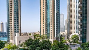 A high-rise residential building with multiple balconies, surrounded by lush greenery and a clear sky.