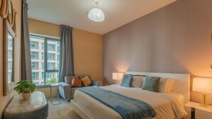 A hotel room with a large bed, bedside tables, a desk, and a window with curtains.