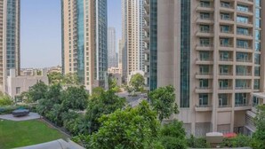 A high-rise residential building with multiple balconies, surrounded by greenery and other high-rise buildings.