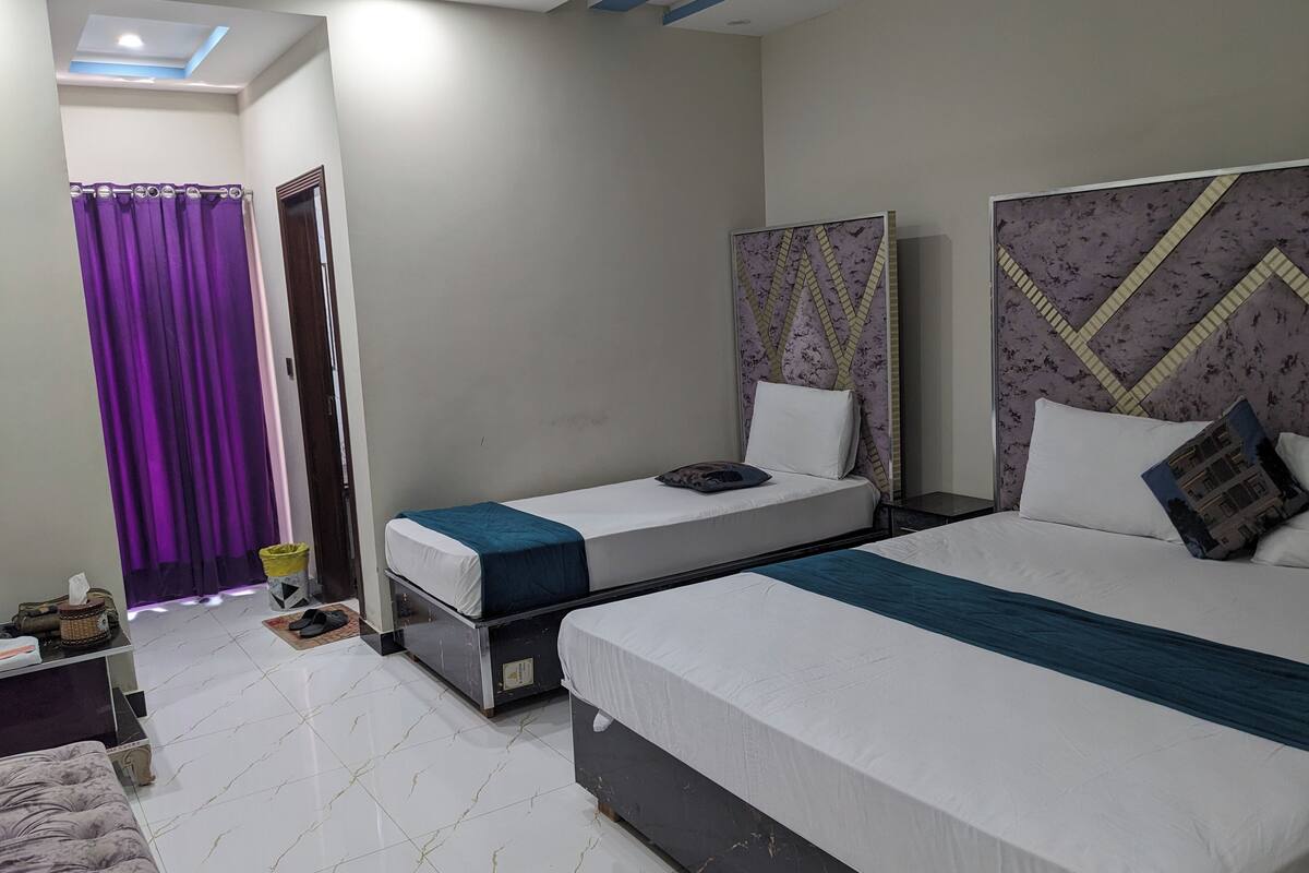 A hotel room with two single beds, a large bed, a ceiling light, and a purple curtain.