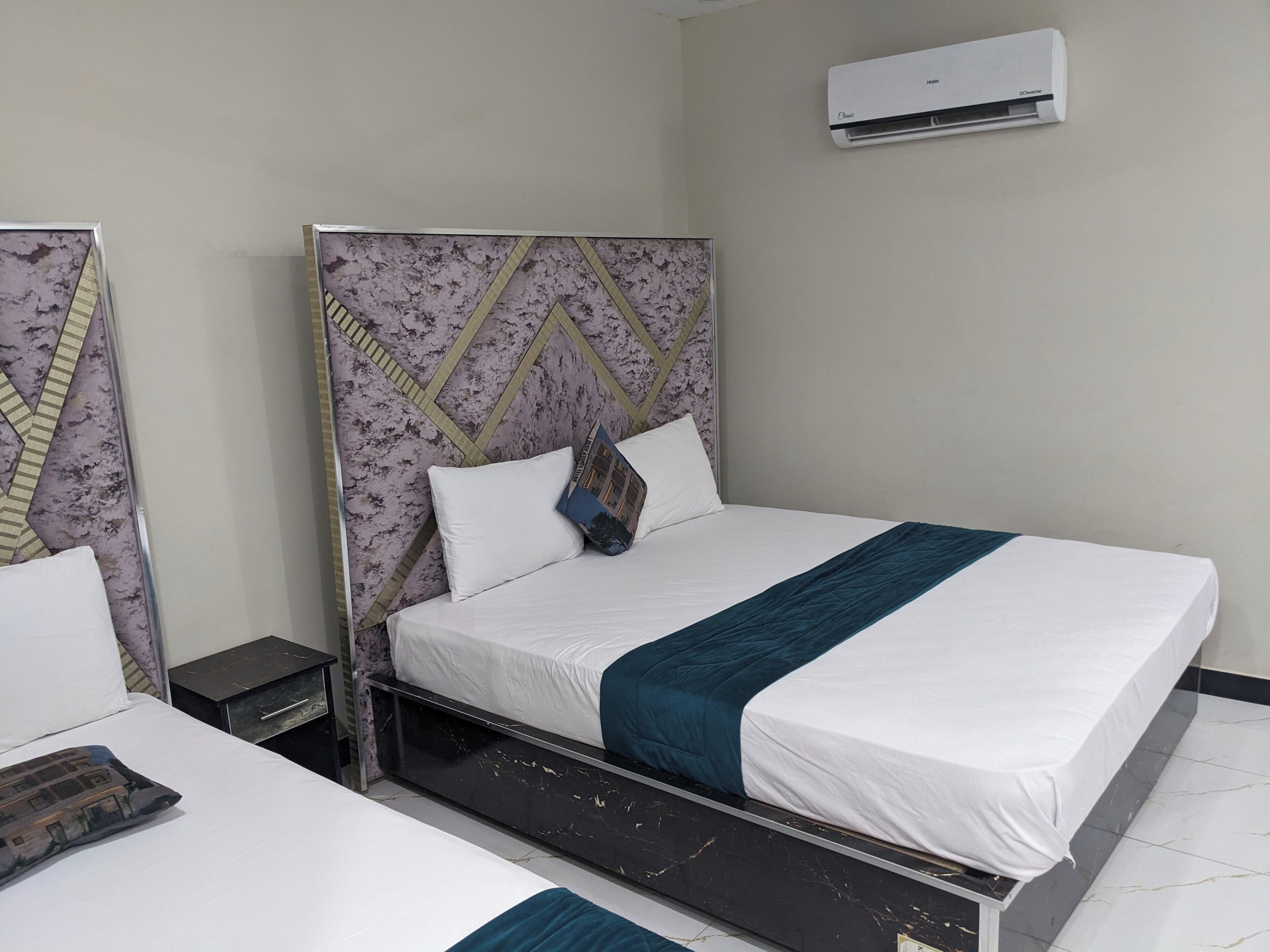 A hotel room with a bed, a nightstand, an air conditioning unit, and a mirror.
