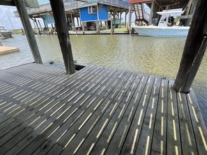 Una terraza de madera con vista a una casa azul y un barco al fondo.