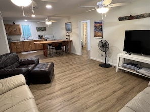 A modern living room with a large TV, leather sofas, a dining area, and a kitchen in the background. - Cheniere - Boat Access - Island Realty (Grand Isle)