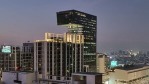 A high-rise building with a unique rooftop structure, surrounded by other tall buildings and a busy street below. - Cozy amazing view loft condo in Asoke Rama9 next to MRT (Huai Khwang)