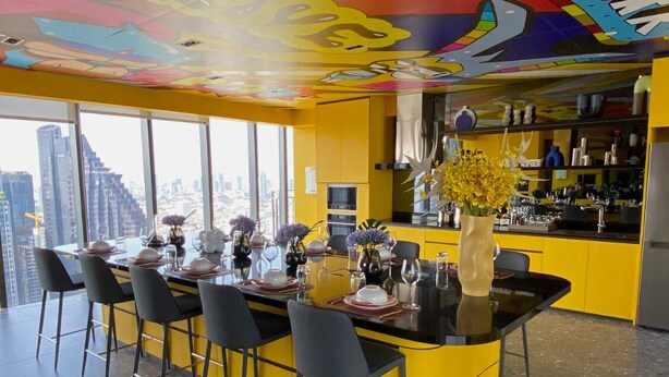 A modern kitchen with yellow cabinets, a bar area, and a dining space with a city view. - Cozy amazing view loft condo in Asoke Rama9 next to MRT (Huai Khwang)