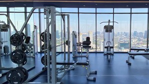 A gym with weightlifting equipment and large windows offering a city view. - Cozy amazing view loft condo in Asoke Rama9 next to MRT (Huai Khwang)