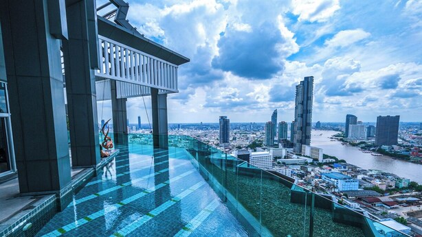 Piscina infinita en la azotea con barandilla de vidrio, con vistas a un paisaje urbano y un río.