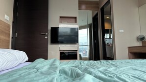 Una habitación de hotel con cama, televisor en la pared, ventana y puerta.