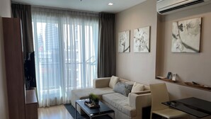 Una sala moderna con sofá, mesa de centro y televisor. Hay cortinas, cuadros en la pared y un equipo de aire acondicionado.