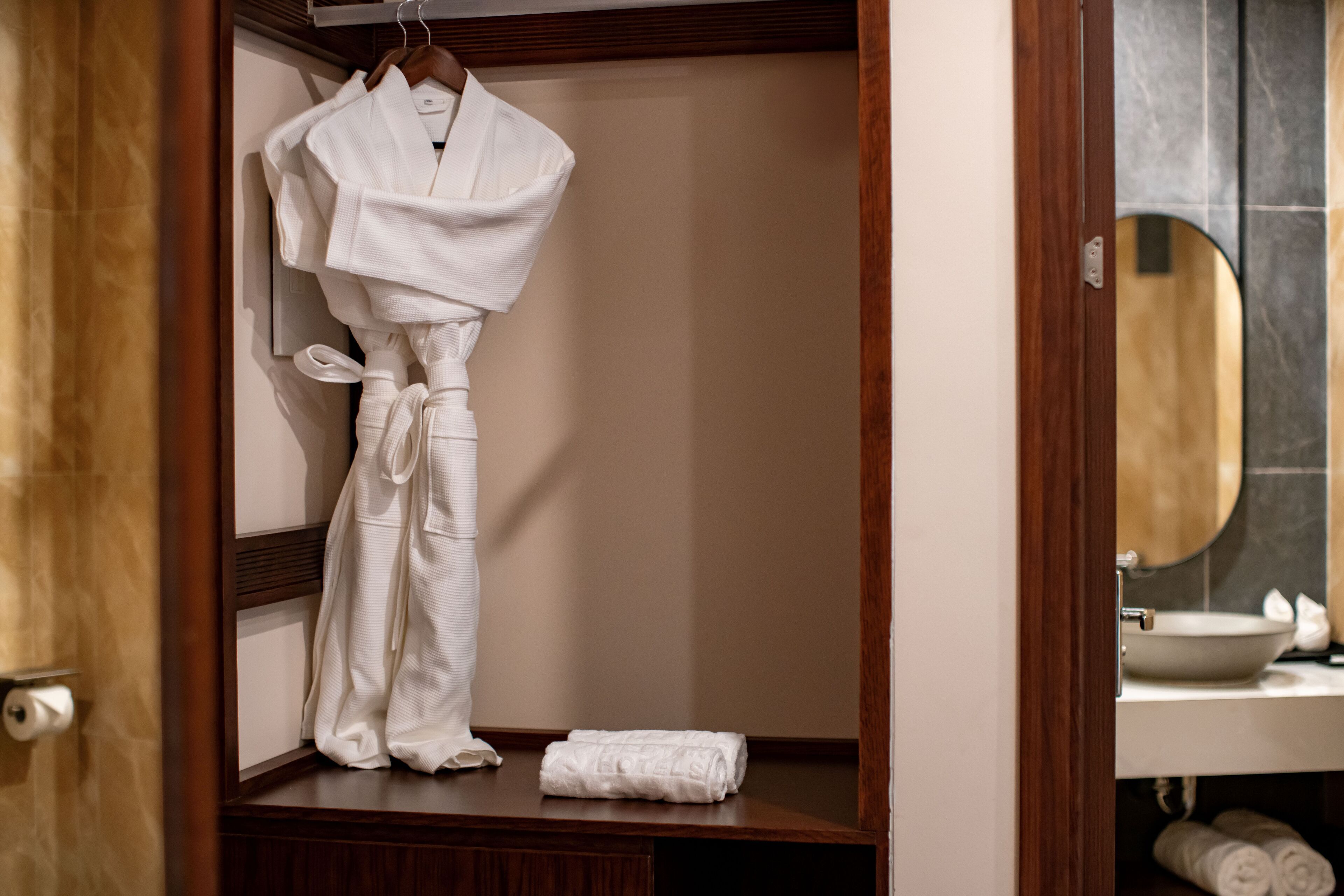 A bathroom with a wooden vanity, a mirror, and a towel rack with a white robe hanging.