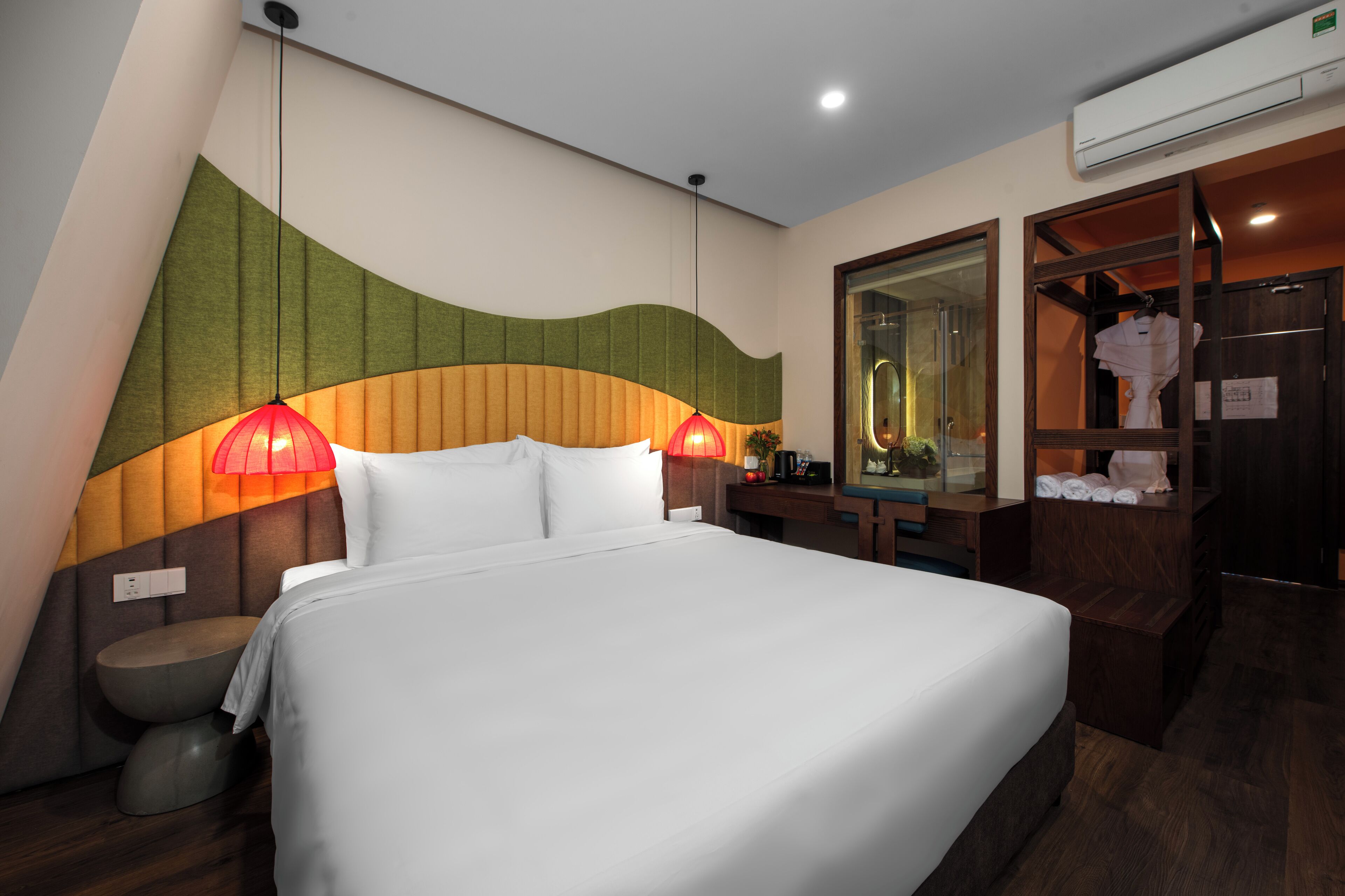 A modern hotel room with a large bed, two bedside lamps, a wooden headboard, a mirror, and a wardrobe.