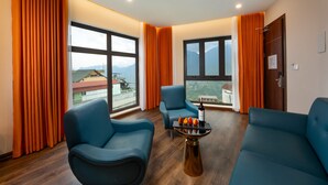 Una habitación moderna con dos sofás azules, una mesita con una botella y fruta, y ventanas grandes con cortinas.