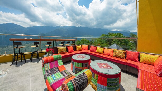 Una terraza en la azotea con un sofá rojo, cojines de colores y dos mesas redondas.