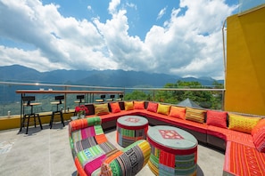 Una terraza en la azotea con un sofá rojo, cojines de colores y dos mesas redondas.